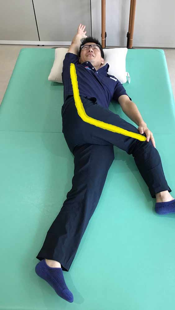 仰向けになり右ひざを立てて、その右ひざを左に倒して右手は万歳でストレッチ